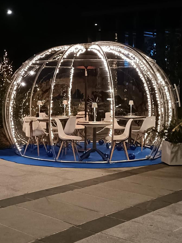 Illuminata bubble room all'esterno con tavolini e sedie all'interno di notte